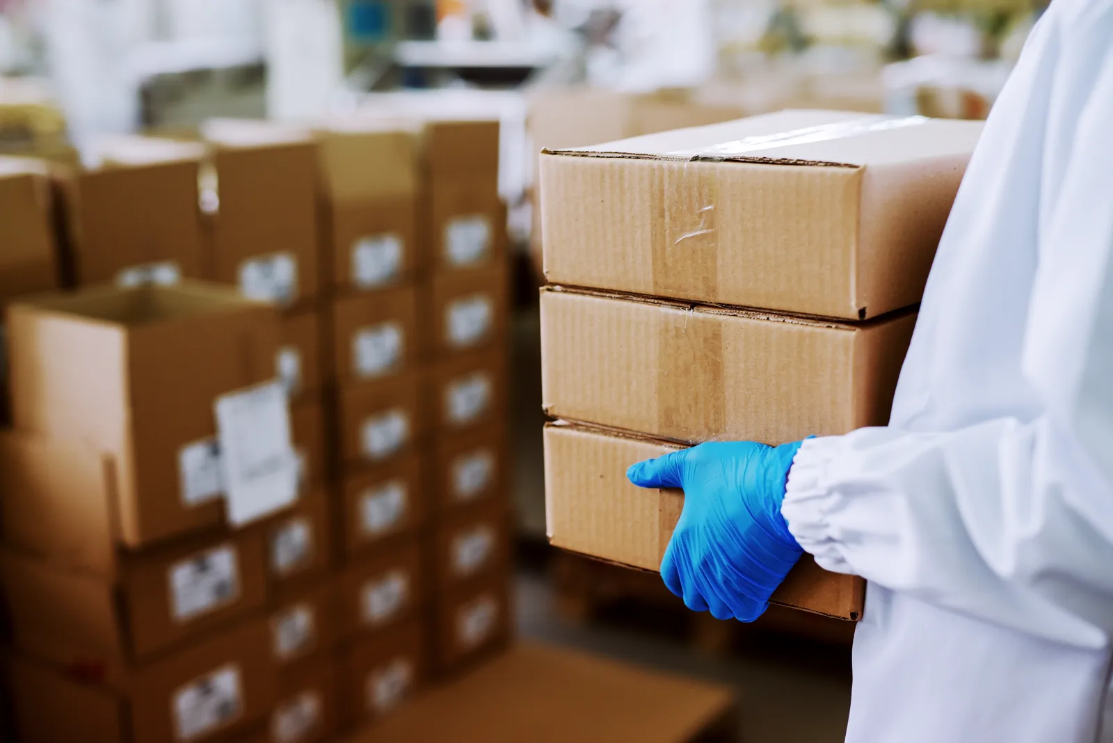 Gloved hands carrying stacked kraft shipping boxes in a warehouse